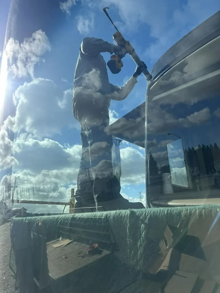 Technician installing a new RV windshield, reflected in the glass